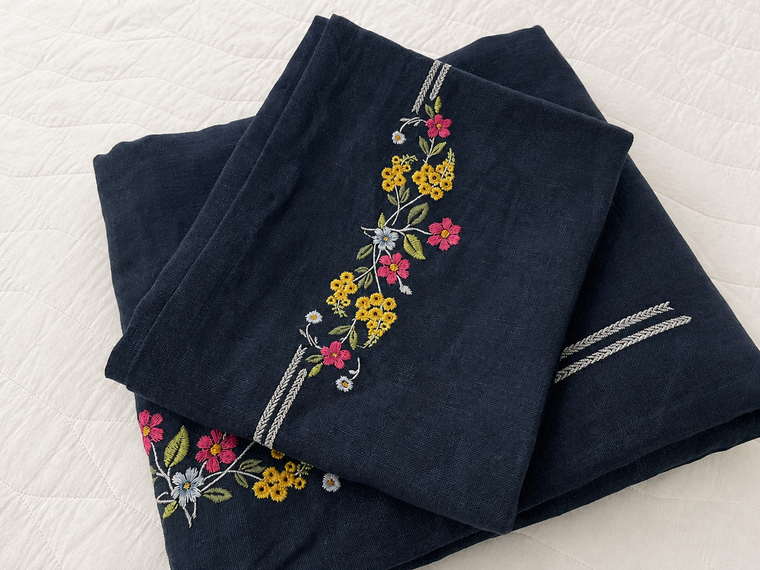 Folded deep navy bed linens with multicolor floral embroidery on white quilted bedding