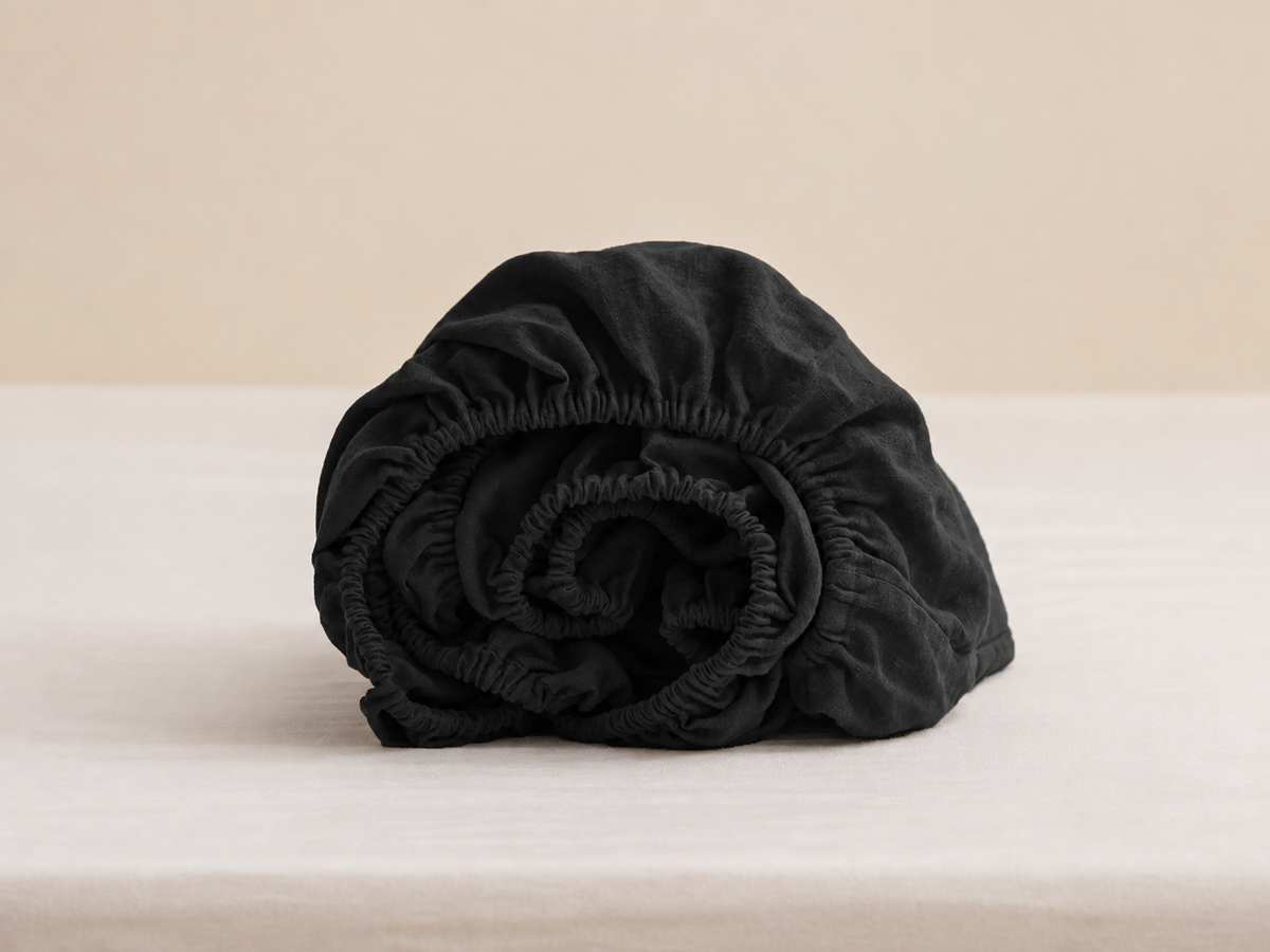 Rolled black fitted sheet showing gathered elastic edges and fabric texture