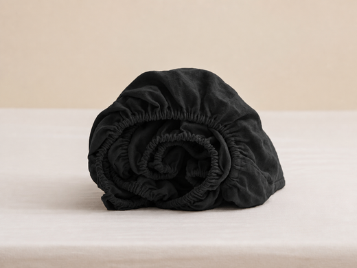Rolled black fitted sheet showing gathered elastic edges and fabric texture
