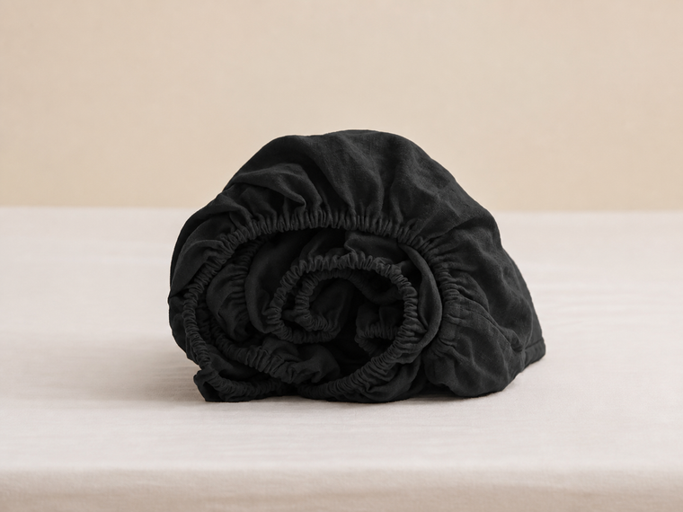 Rolled black fitted sheet showing gathered elastic edges and fabric texture