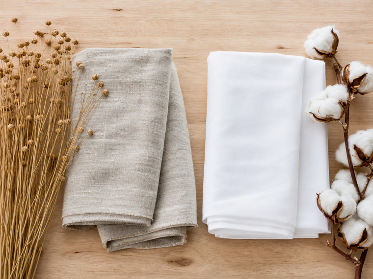 Flax stems and textured linen fabric beside cotton bolls and smooth cotton fabric